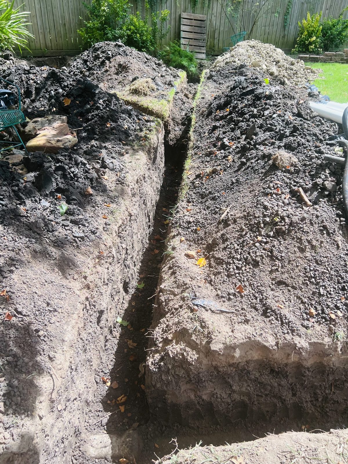A deep, hand-dug trench across a back yard, opened to replace the sewer line.
