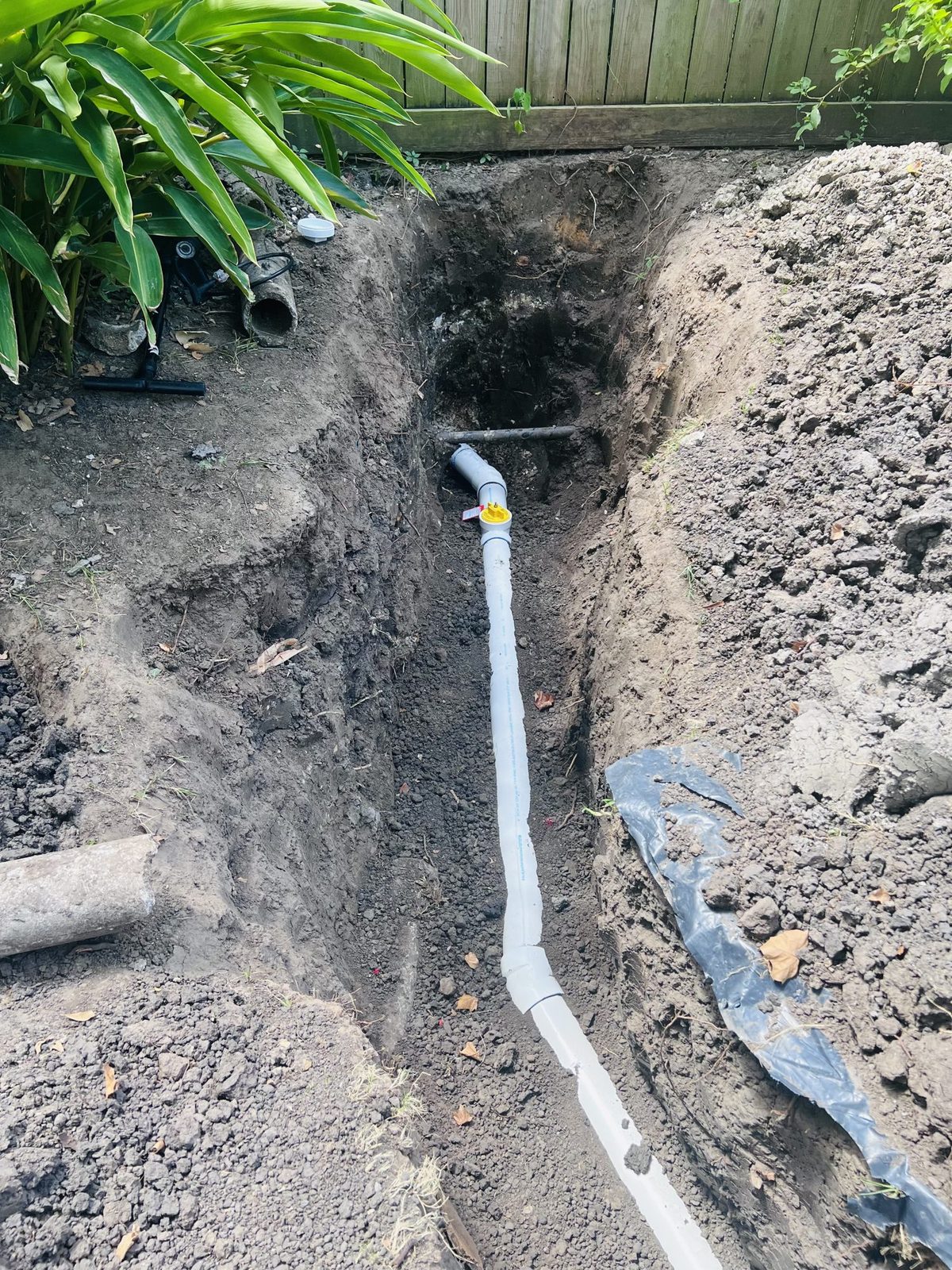 A new sewer line in an open trench with a yellow test plug in place, waiting for its test and inspection before backfill.