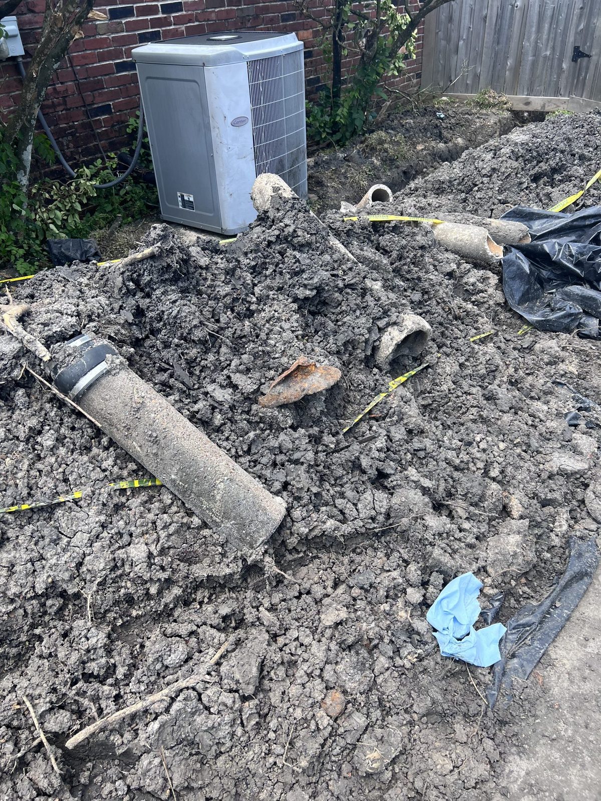 Sections of an old sewer line dug out of a Houston side yard, with a rusted piece of cast iron in the spoil pile.
